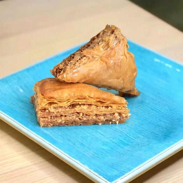 Two pieces of golden-brown baklava, one stacked on top of the other, on a bright blue plate.