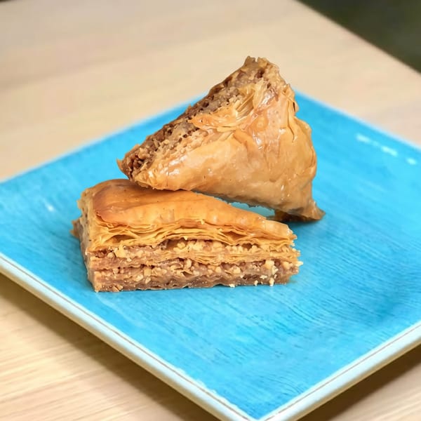 Two triangular pieces of baklava, one stacked on the other, on a blue plate.