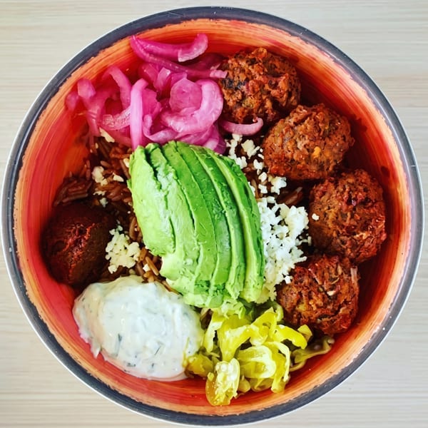 A colorful bowl of falafel, rice, avocado, pickled onions, feta, tzatziki, and banana peppers.