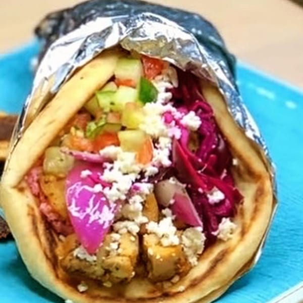 A colorful gyro with chicken, feta, red cabbage, and vegetables, partially wrapped in foil.