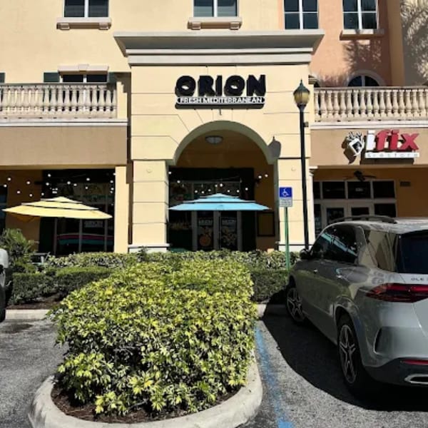 Orion Fresh Mediterranean restaurant exterior with outdoor seating, umbrellas, and a parked car.