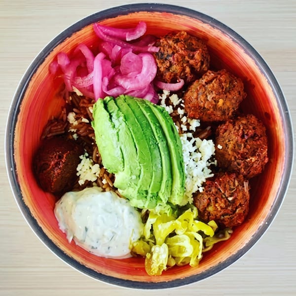 Overhead view of a colorful bowl with falafel, avocado, pickled onions, feta, and sauce.