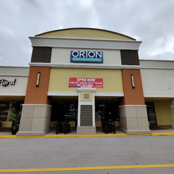 The exterior of Orion Fresh Mediterranean restaurant with an "Open Now" banner and outdoor seating.