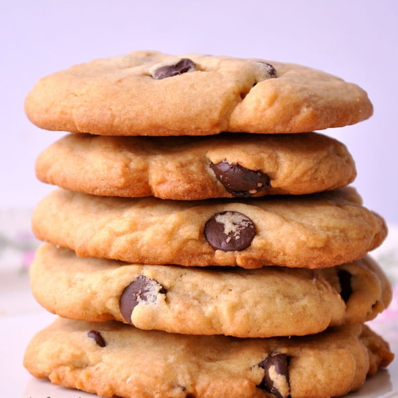 A tall stack of five golden-brown chocolate chip cookies with visible chocolate chunks.
