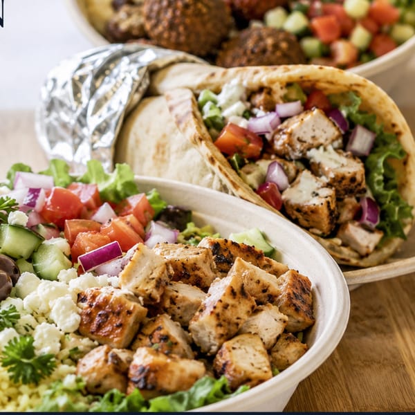 Grilled chicken bowl with salad, a chicken pita wrap, and falafel in the background.