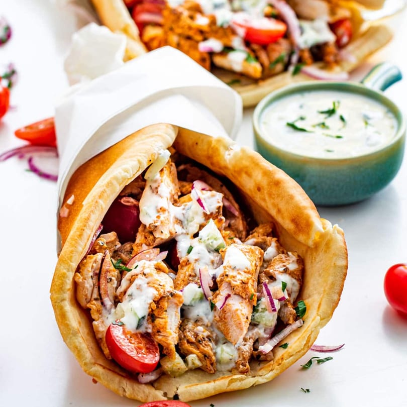 Chicken gyros with tomatoes, red onions, and tzatziki sauce, with a side of sauce.