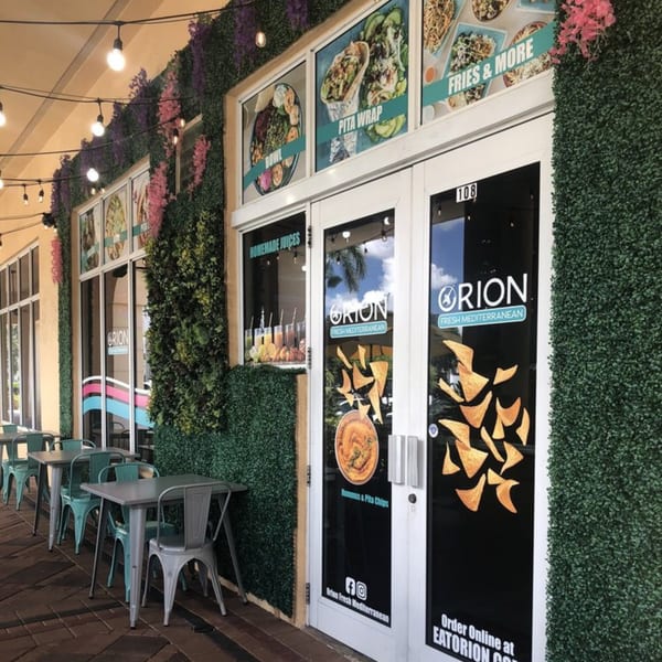 Orion Fresh Mediterranean restaurant exterior with outdoor seating, green foliage walls, and menu displays.