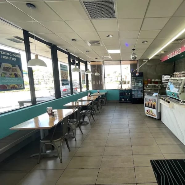 Interior of a restaurant with rows of tables and chairs next to large windows, and a counter area.
